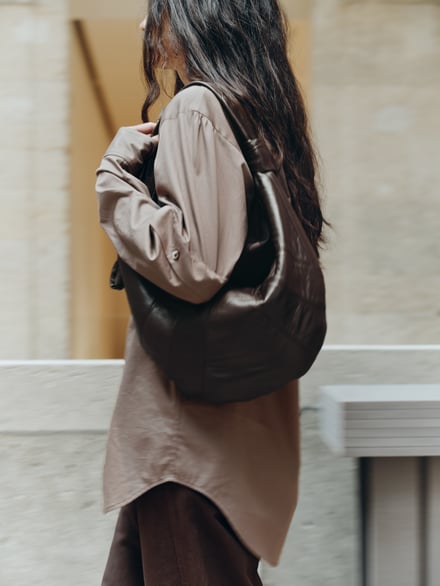 ダークブラウンのレザーのバッグを肩に掛けたロングヘアの女性